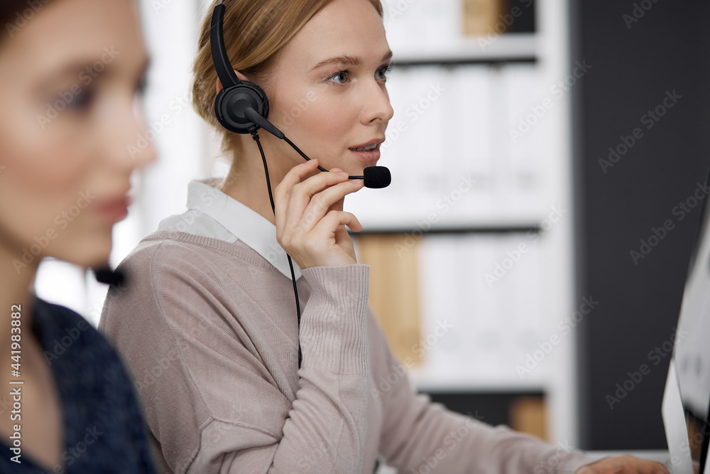 Friendly businesswoman talking by headset while sitting in office. Call center and diverse people group in business Friendly businesswoman talking by headset while sitting in office. Call center and diverse people group in business
