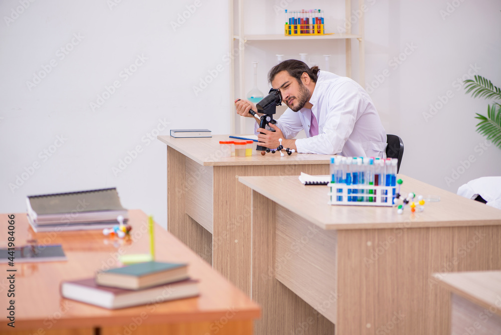 Obraz premium Young male chemist sitting at the desk in the classroom