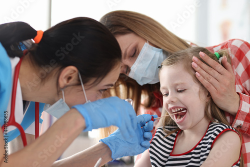 Doctor in protective medical mask taking buccal swab from little girl with cotton swab photo