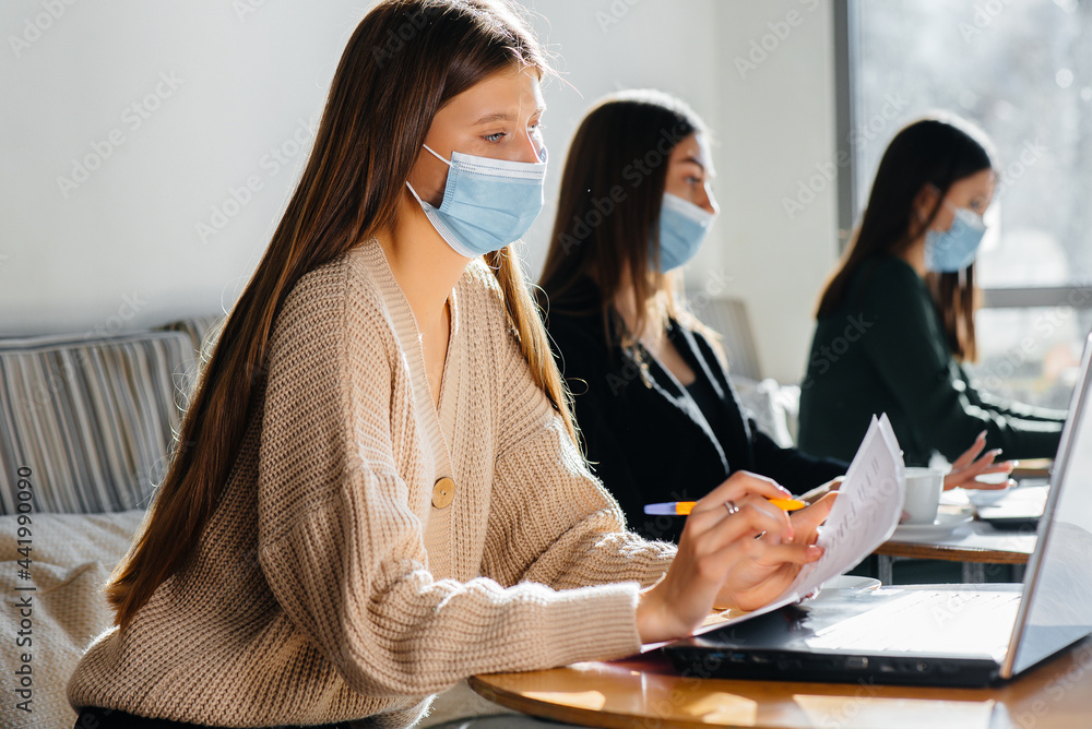 A group of masked girls keep a social distance in a cafe when working on laptops. A group of masked girls keep a social distance in a cafe when working on laptops.