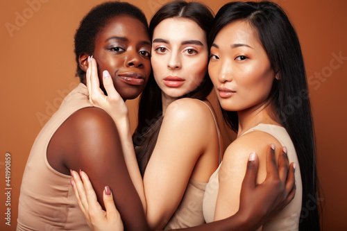 young pretty caucasian, afro, asian, scandinavian woman posing cheerful together on brown background, lifestyle diverse nationality people concept