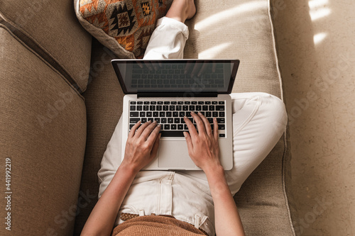 Fotografija Young woman workin on laptop computer lying on the couch