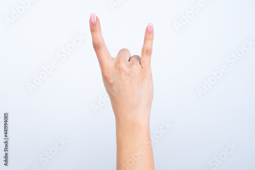 Woman's hand with pink manicure over isolated white background showing horns © Roquillo