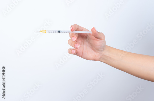 Woman's hand with pink manicure holding a syringe over white studio background.