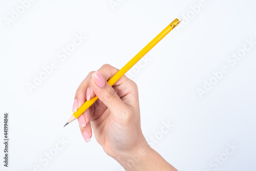 Woman's hand with pink manicure holding a yellow pencil over white studio background. 