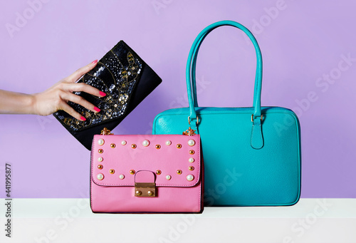 Colourful bags purses on purple background. 
Woman hand with red manicured nails holding wallet.