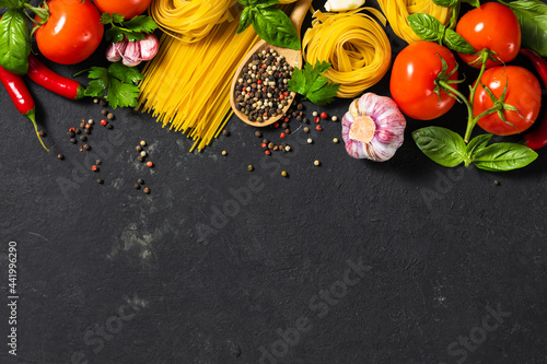 Italian food ingredients with pasta, tomatoes, pepper, garlic and parsley on dark background with copy space, top view © kucherav