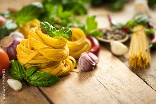 Tagliatelle and pasta on wooden table with basil leaf, pepper, garlic and parsley with copy space
