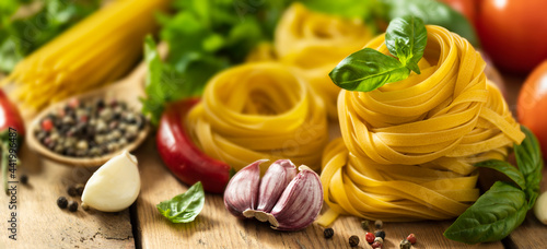 Tagliatelle and pasta on wooden table with basil leaf, pepper, garlic and parsley with copy space photo