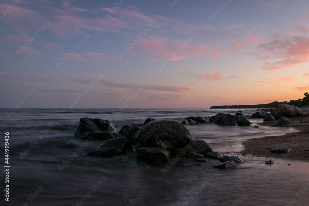 rocky sea shore before sunrise, dark stone silhouettes and colorful sky