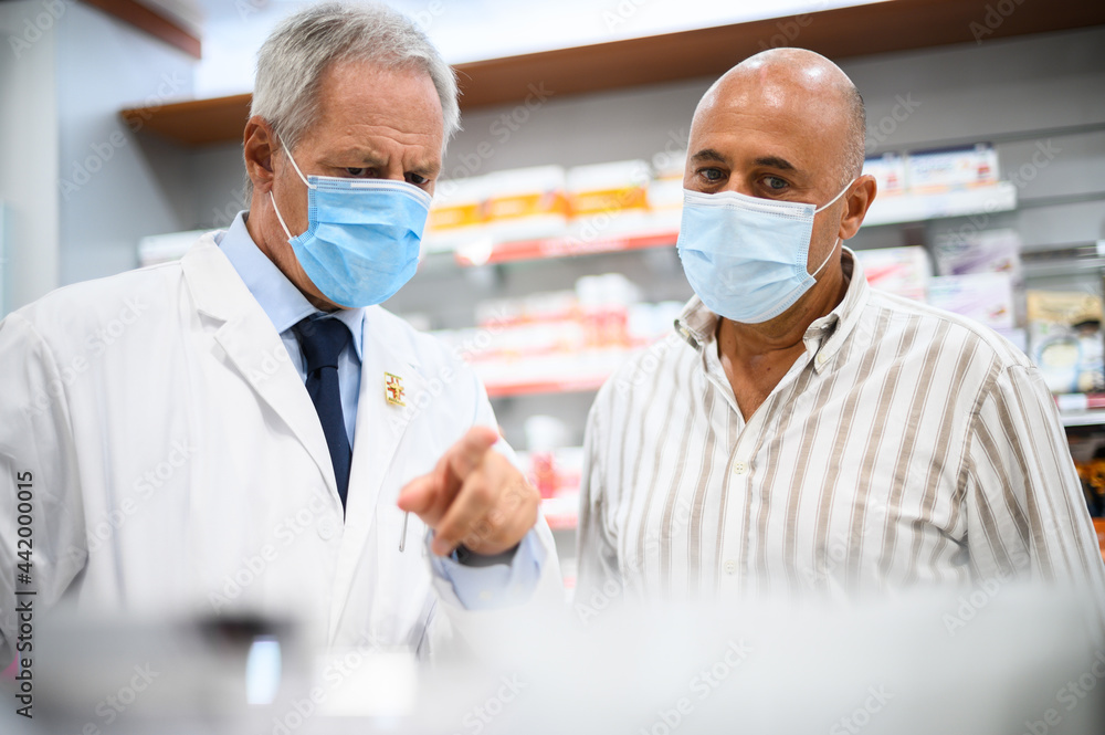 Senior pharmacist dealing with a customer, both of them wearing masks due to coronavirus Senior pharmacist dealing with a customer, both of them wearing masks due to coronavirus