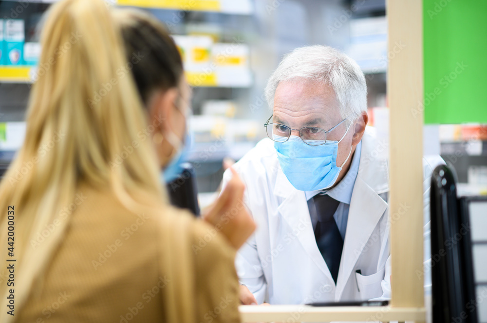 Senior pharmacist dealing with a customer, both of them wearing masks due to coronavirus Senior pharmacist dealing with a customer, both of them wearing masks due to coronavirus