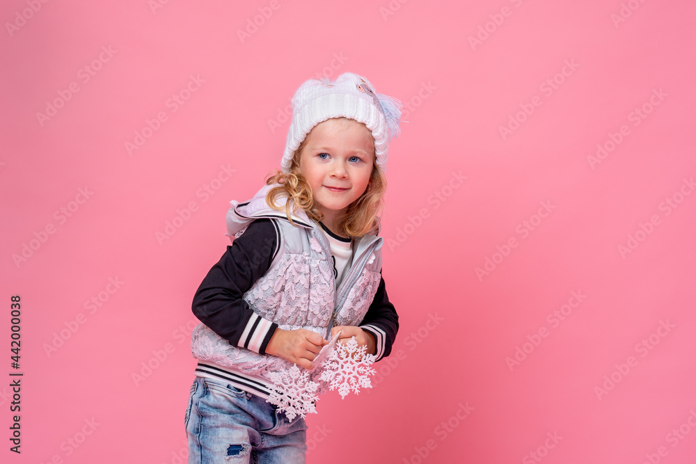 cute little girl in a hat and vest holds Christmas snowflakes on a pink background. the child is happy, having fun and getting ready for Christmas. The advertiser. A place to copy. cute little girl in a hat and vest holds Christmas snowflakes on a pink background. the child is happy, having fun and getting ready for Christmas. The advertiser. A place to copy.