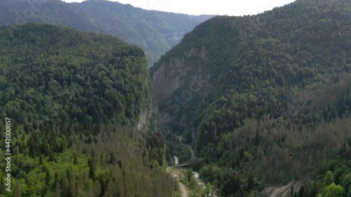 Aerial view from above flying over amazing nature scenery at Abkhazia, Yupsharsky canyon. Natural environment hilly terrain covered by beautiful dense trees with small fast mountain river and bridge photo