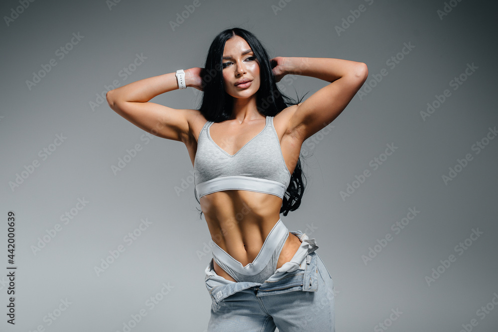 Young sexy brunette posing in lingerie and jeans on a gray background. The perfect athletic figure. Young sexy brunette posing in lingerie and jeans on a gray background. The perfect athletic figure.