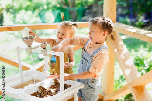 Happy sister kids play with sand and water in sensory baskets on the outdoor sensory table, sensory early development, montessori. Toddler and Big Sister Play with Sand, Soft Focus