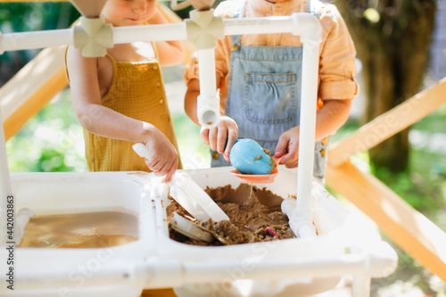 Happy sister kids play with sand and water in sensory baskets on the outdoor sensory table, sensory early development, montessori. Toddler and Big Sister Play with Sand, Soft Focus