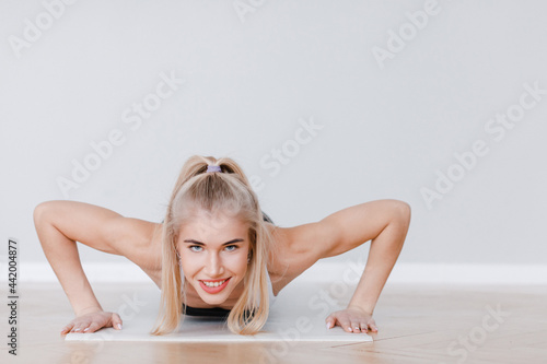 Sporty beautiful blonde is doing push-ups looking at the camera.