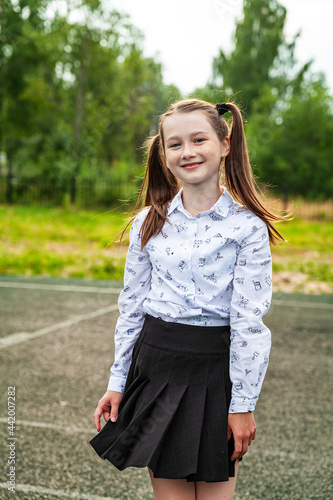 Schoolgirl in white blouse and black skirt , long hair is taken in tails, school, education, street, school stadium