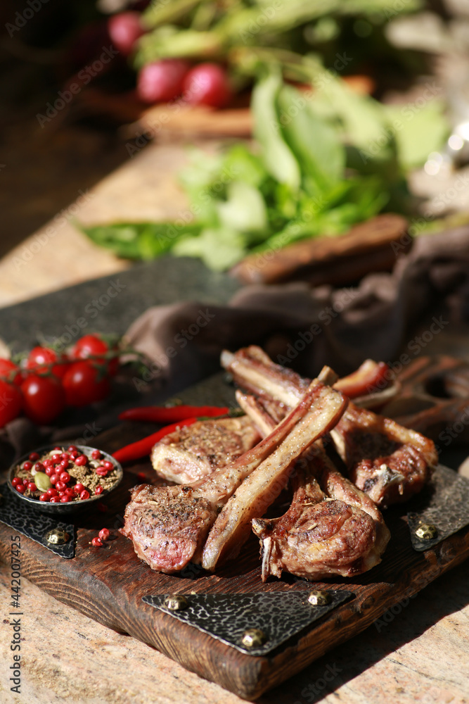 Grilled lamb ribs with spices and fresh vegetables and herbs on a wooden board. Picnic, outdoor, sunlight,a square of lamb. Rustic. Background image, copy space