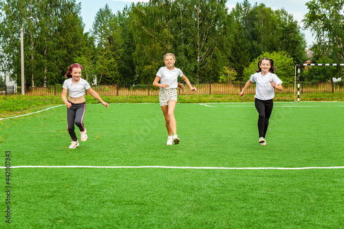 Three cheerful girls run a race on the playground. Warm-up, running, exercise, open air, outdoors