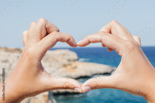 Heart shape with hands on a background of blue ocean and sand rocks close up