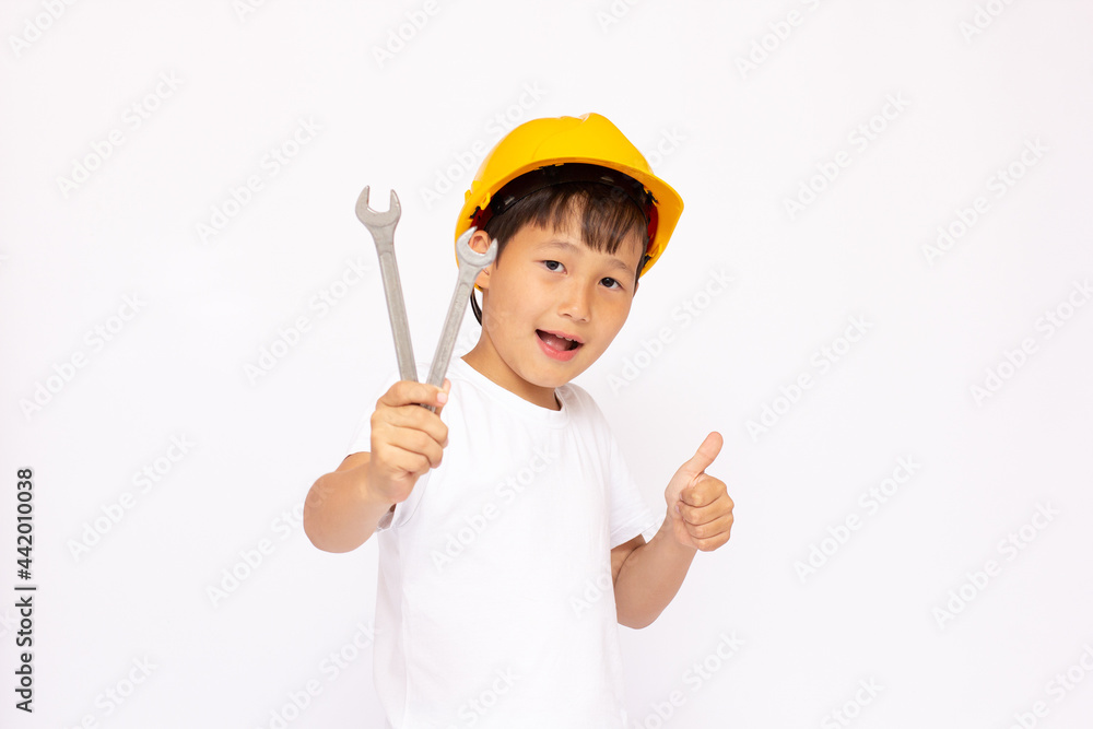 A cute boy in a hard hat looks to the right, in the hands of a child with a wrench and a hammer. The concept of the importance of using personal protective equipment and special tools A cute boy in a hard hat looks to the right, in the hands of a child with a wrench and a hammer. The concept of the importance of using personal protective equipment and special tools