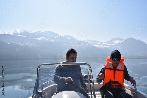 Father explaining his son how to drive a motorboat on lake Lucerne. The son is wearing orange life jacket. There is a lot of copy space on the background.