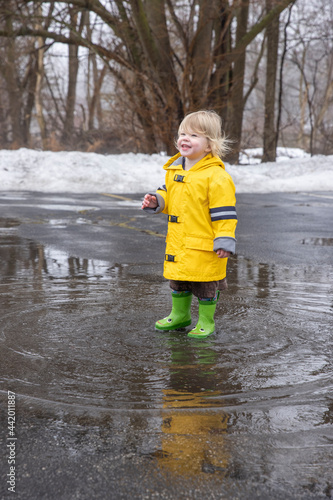 Fototapeta Naklejka Na Ścianę i Meble -  Toddler girl splashing in puddles wearing a yellow raincoat 