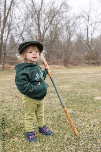 Toddler girl in an Irish walking cap and walking stick looking off in the distance with her hand in her pocket photo