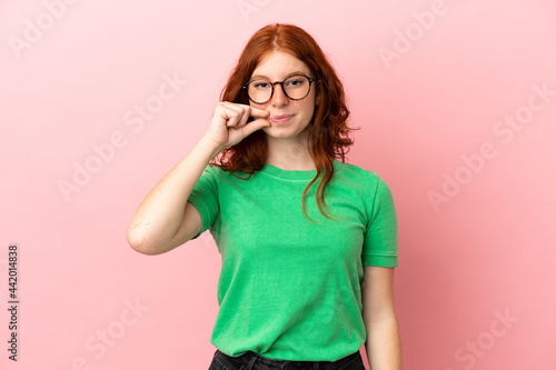 Teenager redhead girl over isolated pink background showing a sign of silence gesture