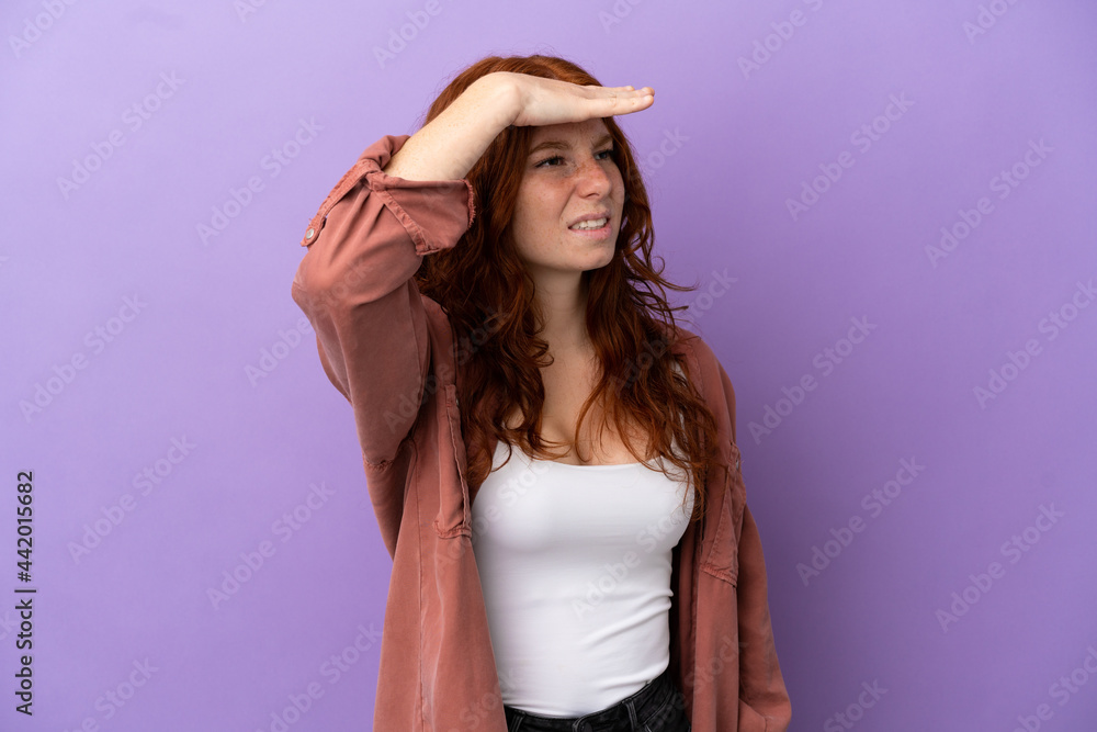 Teenager redhead girl over isolated purple background looking far away with hand to look something Teenager redhead girl over isolated purple background looking far away with hand to look something