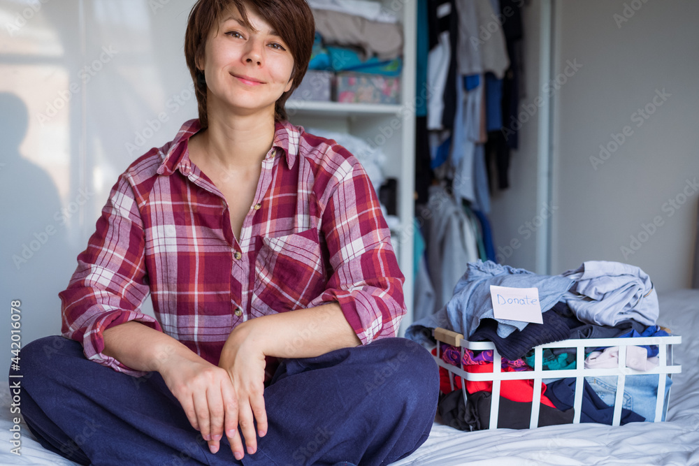 Smiling Woman with selected clothes from her wardrobe for donating to a Charity. Decluttering Clothes, Sorting, And Cleaning Up. Reuse, second-hand concept. Conscious consumer, sustainability. Smiling Woman with selected clothes from her wardrobe for donating to a Charity. Decluttering Clothes, Sorting, And Cleaning Up. Reuse, second-hand concept. Conscious consumer, sustainability.