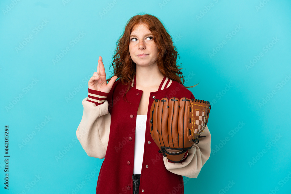 Teenager redhead girl with baseball glove isolated on blue background with fingers crossing and wishing the best Teenager redhead girl with baseball glove isolated on blue background with fingers crossing and wishing the best