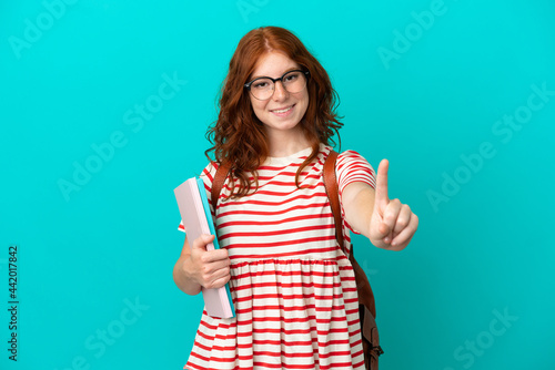 Student teenager redhead girl isolated on blue background showing and lifting a finger