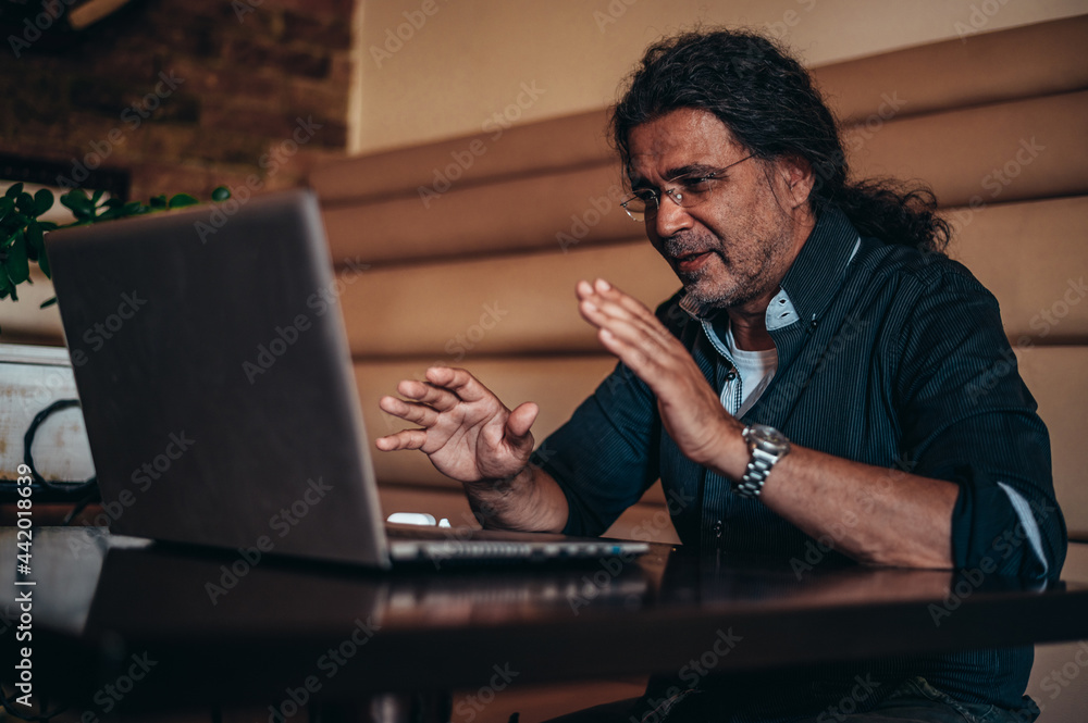 Senior hispanic cuban man using his laptop for an online video call in a cafe Senior hispanic cuban man using his laptop for an online video call in a cafe