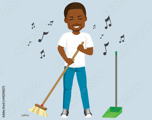 Young black man singing and sweeping floor doing house chores