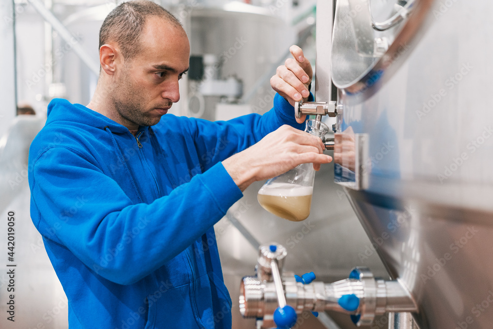 Engineer with glass of liquid near fermentation tank in brewery Engineer with glass of liquid near fermentation tank in brewery
