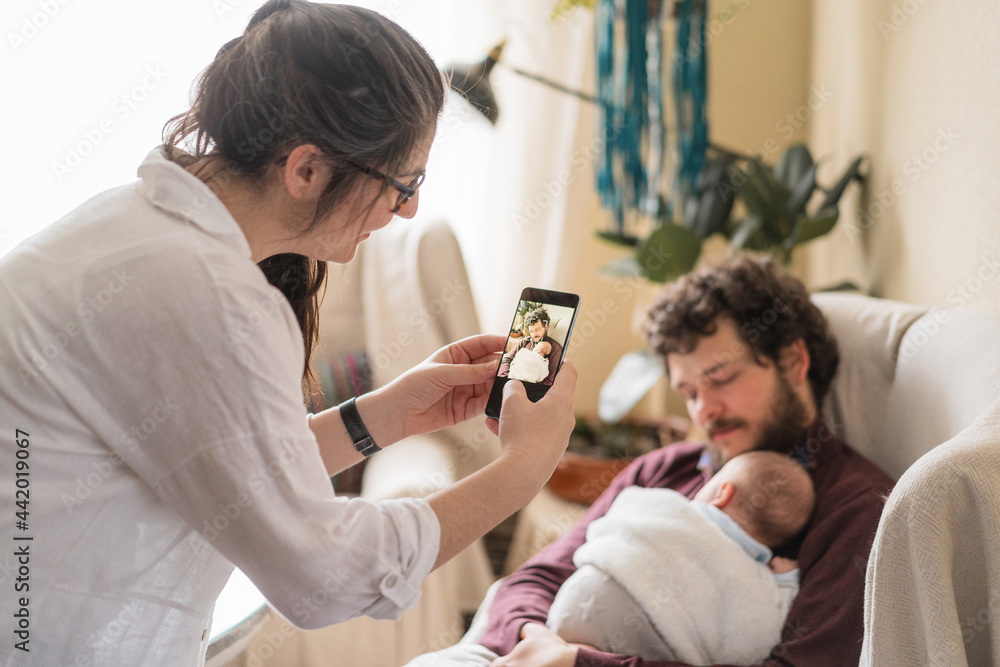 Smiling woman taking photo of husband with baby on smartphone Smiling woman taking photo of husband with baby on smartphone