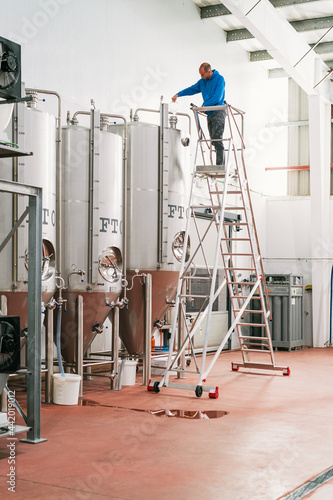 Brewer on ladder filling fermentation reservoir in beer factory