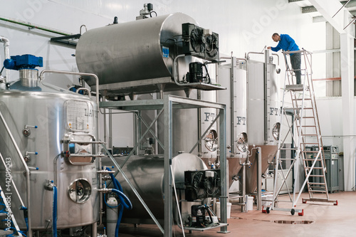 Brewer on ladder filling fermentation reservoir in beer factory photo