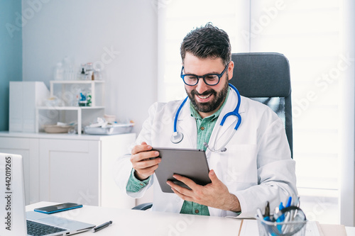 Smiling physician with tablet during video call in clinic photo