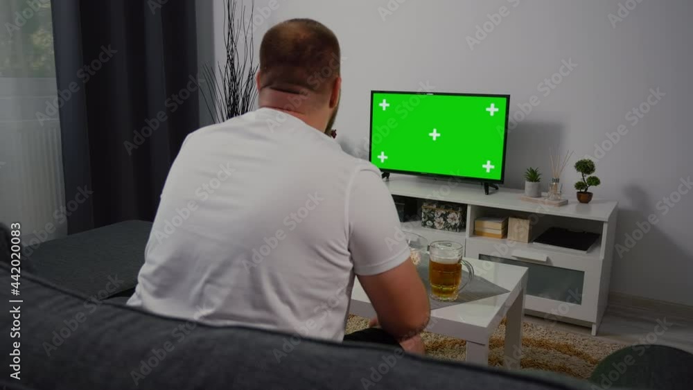 At Home male Soccer Fan Sitting on a Couch Watching Green Screen Chroma Key Screen. Support favorite Team Football Sports Team to Win Championship. Shot Over the Shoulder Green Screen Tv. At Home male Soccer Fan Sitting on a Couch Watching Green Screen Chroma Key Screen. Support favorite Team Football Sports Team to Win Championship. Shot Over the Shoulder Green Screen Tv.