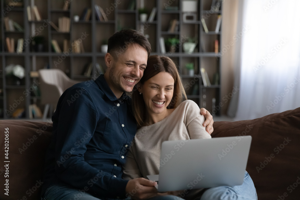 Smiling young man and woman relax on sofa at home watch video or movie laughing. Happy millennial Caucasian couple rest on couch in living room talk on webcam call on laptop. Smiling young man and woman relax on sofa at home watch video or movie laughing. Happy millennial Caucasian couple rest on couch in living room talk on webcam call on laptop.
