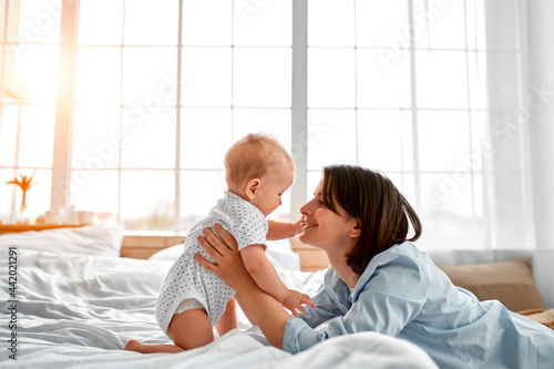Loving mom carying of her newborn baby at home.Mom and baby boy playing in sunny bedroom. Parent and little kid relaxing at home. Family having fun together. Childcare, maternity concept.