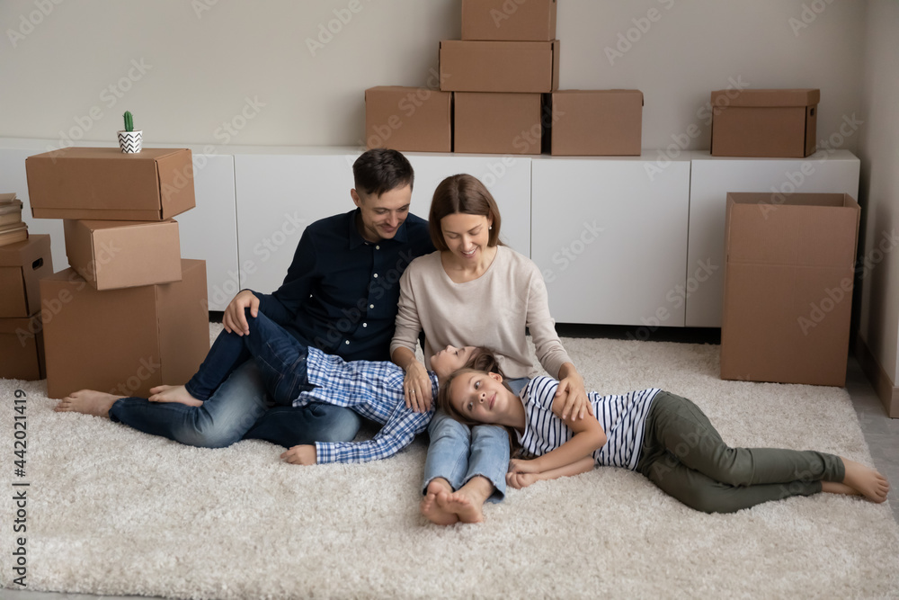 Happy young Caucasian parents with two teenage children sit on floor in new home relax on moving day. Smiling family with teen kids rest in cozy living room relocate together. Rent, rental concept. Happy young Caucasian parents with two teenage children sit on floor in new home relax on moving day. Smiling family with teen kids rest in cozy living room relocate together. Rent, rental concept.