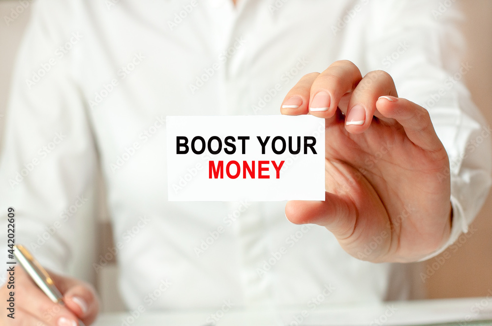 A woman in a white shirt holds a piece of paper with the text: BOOST YOUR MONEY. Business concept. A woman in a white shirt holds a piece of paper with the text: BOOST YOUR MONEY. Business concept.