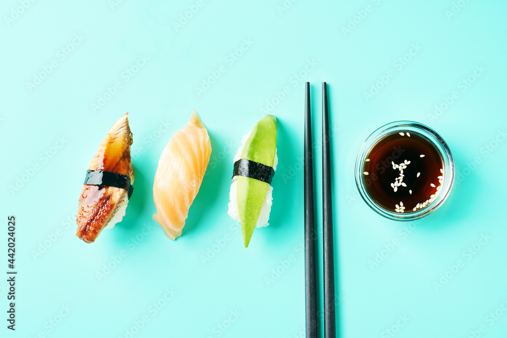 Top view modern minimal style of sushi set anago unagi (eel) sushi with nori (seaweed), nigiri salmon, avocado top on rice, soy sauce and black chopsticks on blue turquoise background with copyspase. Top view modern minimal style of sushi set anago unagi (eel) sushi with nori (seaweed), nigiri salmon, avocado top on rice, soy sauce and black chopsticks on blue turquoise background with copyspase.