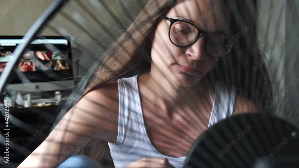 Tired overheated young hipster woman wear glasses suffering from too high temperature in home office sitting in front cooling fan, ventilator. Hot weather. People texting phone check social media. Tired overheated young hipster woman wear glasses suffering from too high temperature in home office sitting in front cooling fan, ventilator. Hot weather. People texting phone check social media.