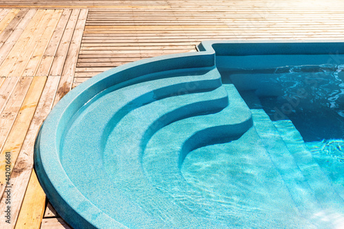 Photography New modern fiberglass plastic swimming pool entrance step with clean fresh refreshing blue water on bright hot summer day at yard or resort hotel spa area